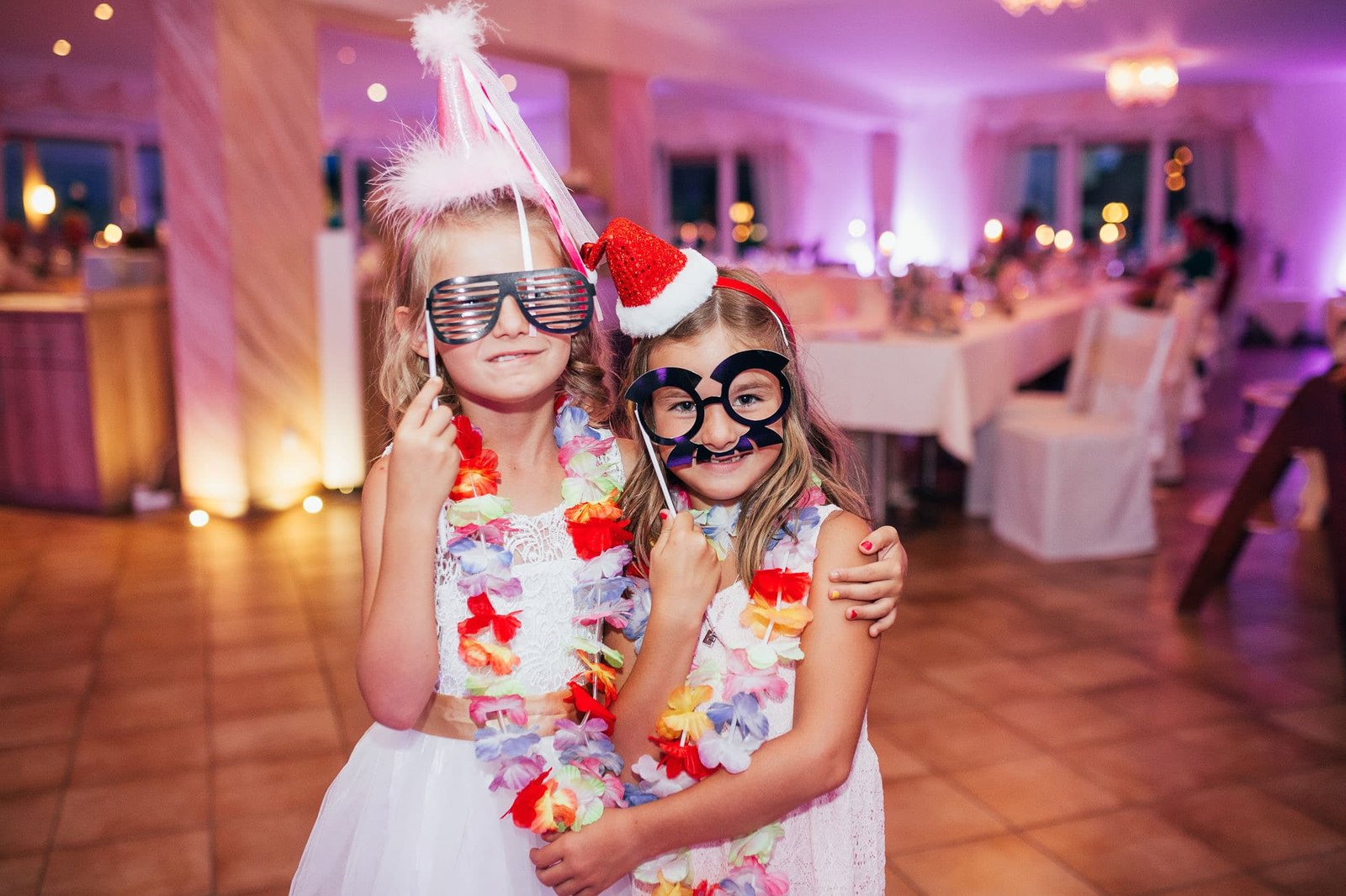Zwei Kinder mit lustigen Party-Accessoires bei einer Hochzeit neben einer modernen Fotobox in Österreich.